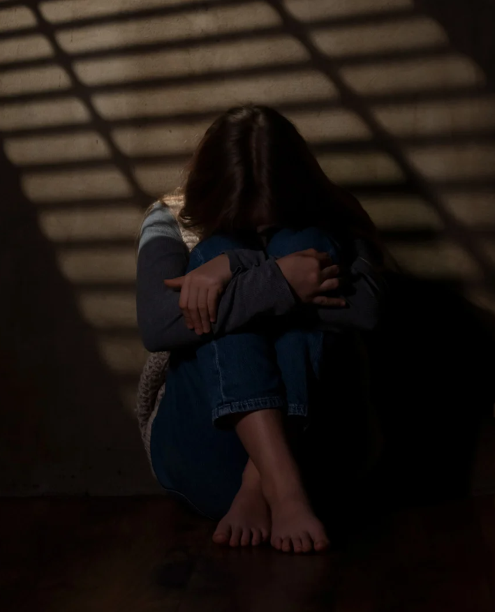어두운 방에서 무릎을 안고 웅크린 여성